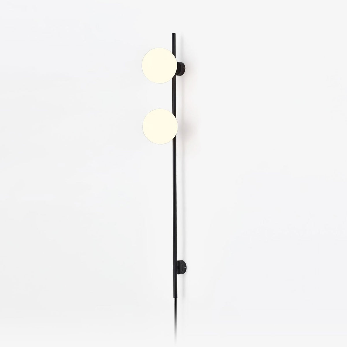 A Clérachic plug-in wall light with two frosted white globes on a slim black rod, with the cord trailing down a plain white wall.