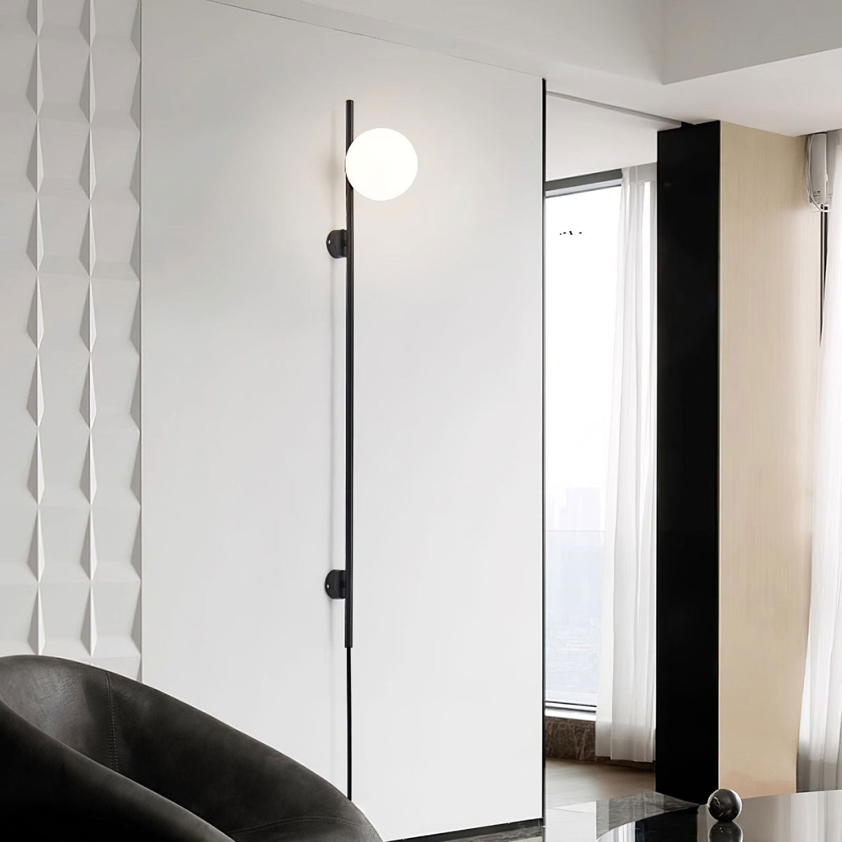 One lit globe near the top of this Clérachic slim black wall light, beside a tall window and a dark leather armchair.