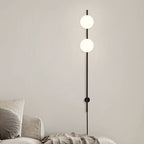 Two lit white globes on this Clérachic black wall light, mounted on a beige wall above a cream sofa and throw.