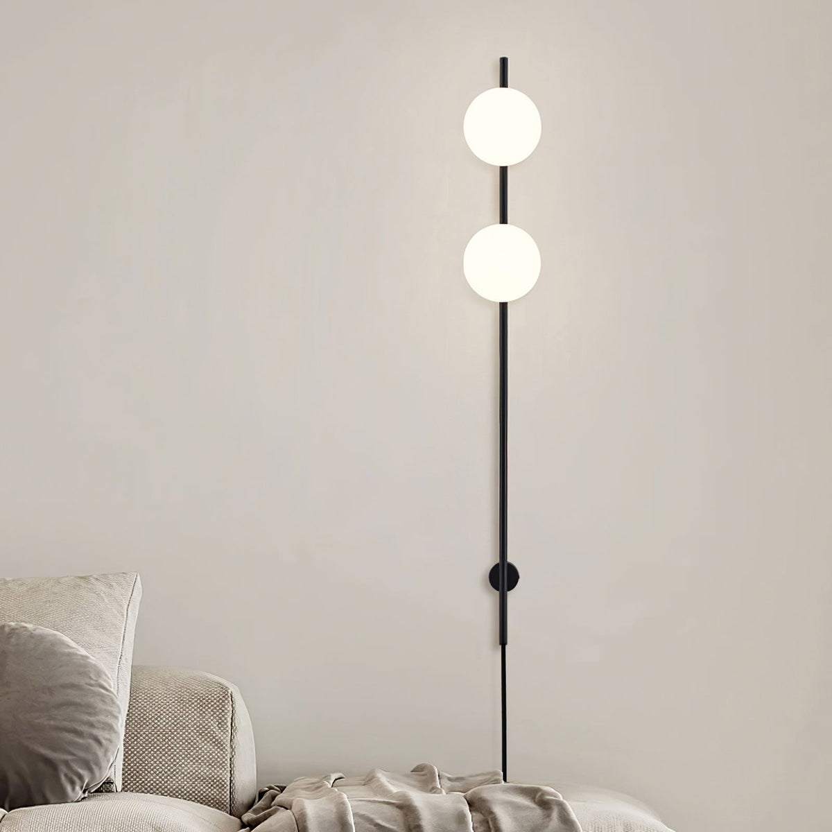Two lit white globes on this Clérachic black wall light, mounted on a beige wall above a cream sofa and throw.