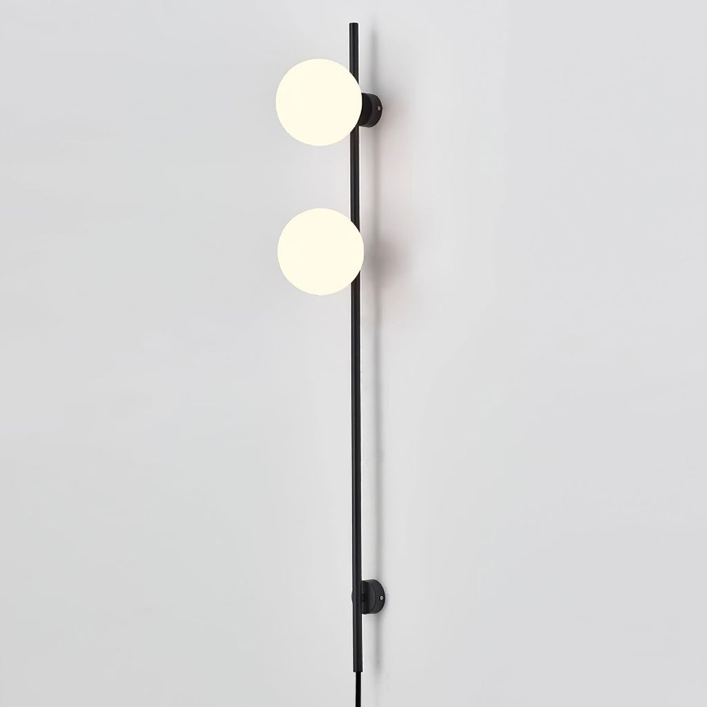 Close view of two glowing globes on this Clérachic slim black wall light, against a pale grey wall with the cord at the base.