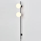 Close view of two glowing globes on this Clérachic slim black wall light, against a pale grey wall with the cord at the base.