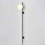 A Clérachic black wall light with one warm globe at the top of its rod, mounted on a pale wall with the cord hanging below.
