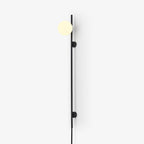 A Clérachic plug-in wall light with a softly lit globe on a thin black rod, with two small mounts, against a bright white wall.