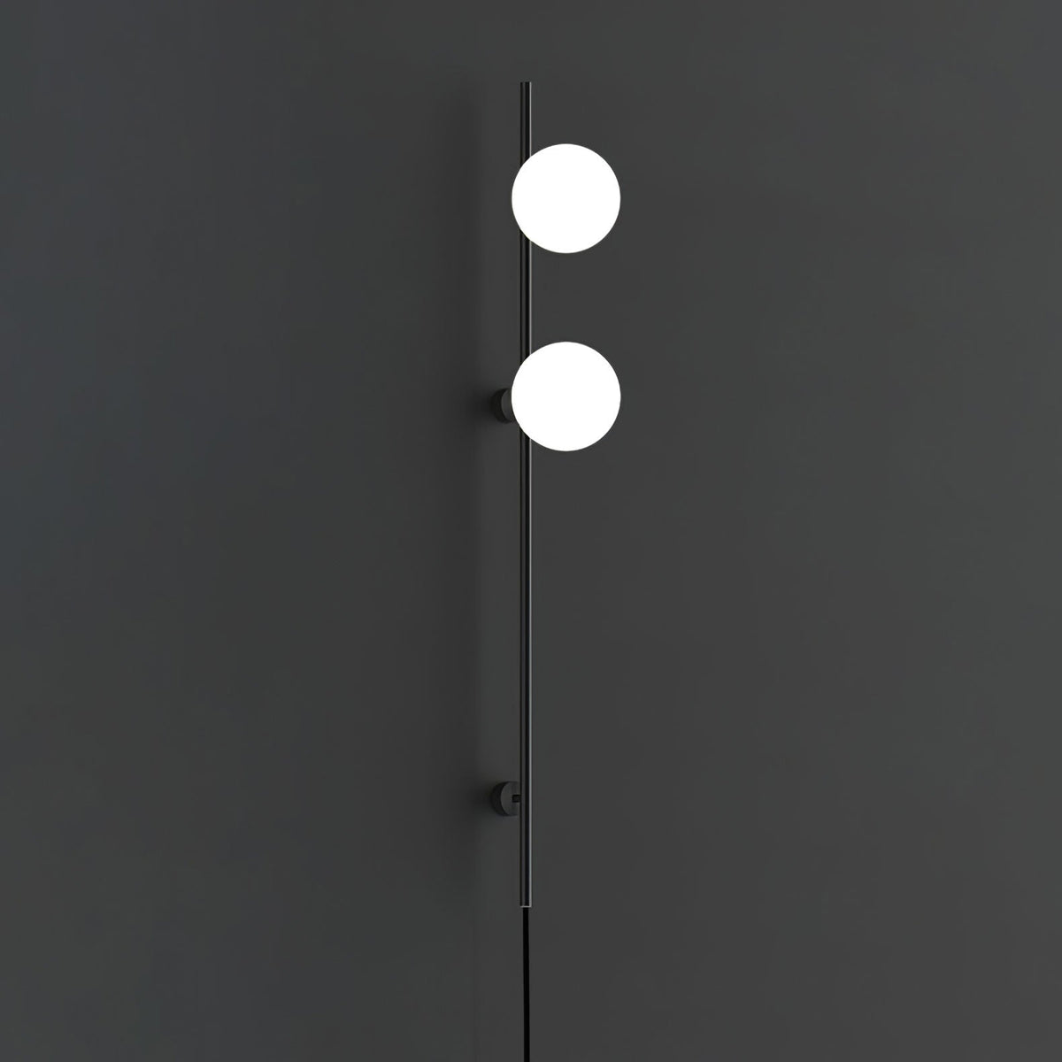 This Clérachic wall light on a charcoal wall, with two bright white globes on a slim black rod and a cord below.