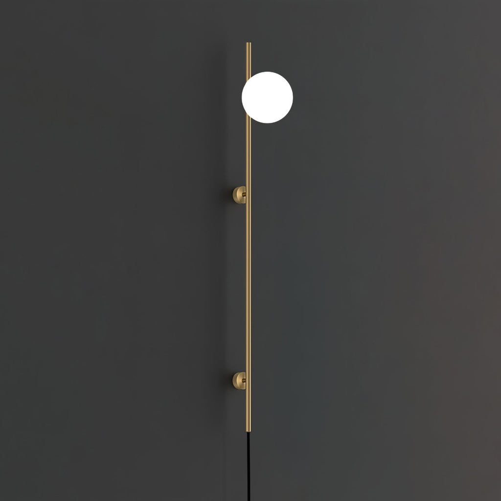A gold-toned version of the Clérachic wall light on a charcoal wall, with one bright white globe on a slim rod and two round mounts.
