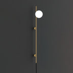 A gold-toned version of the Clérachic wall light on a charcoal wall, with one bright white globe on a slim rod and two round mounts.