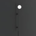 A single bright globe on the slim black rod of this Clérachic wall light, against a dark charcoal wall with two small mounts.