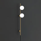 A Clérachic wall light in gold with two bright white globes on a slim rod and two round mounts, against a charcoal wall.