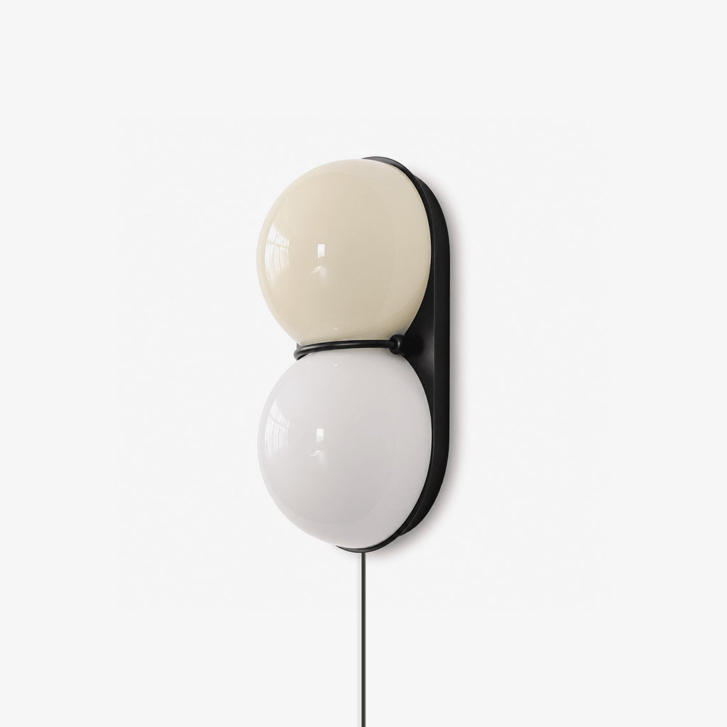 Clérachic wall sconce with two stacked glass globes, cream above and white below, on a black oval backplate with a black cord.