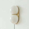 Close, front-on view of a white two-globe Clérachic wall sconce on a brass backplate, joined by a slim brass band.