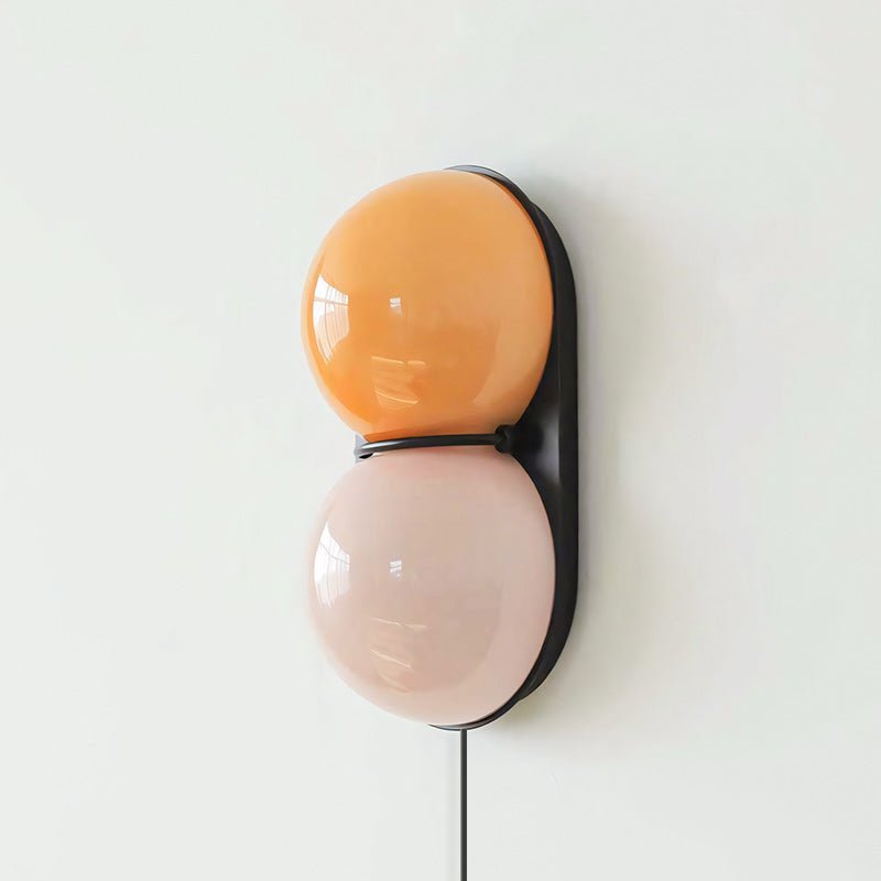 Clérachic wall sconce with an orange globe above a pale pink one on a black oval backplate, seen from a slight angle.