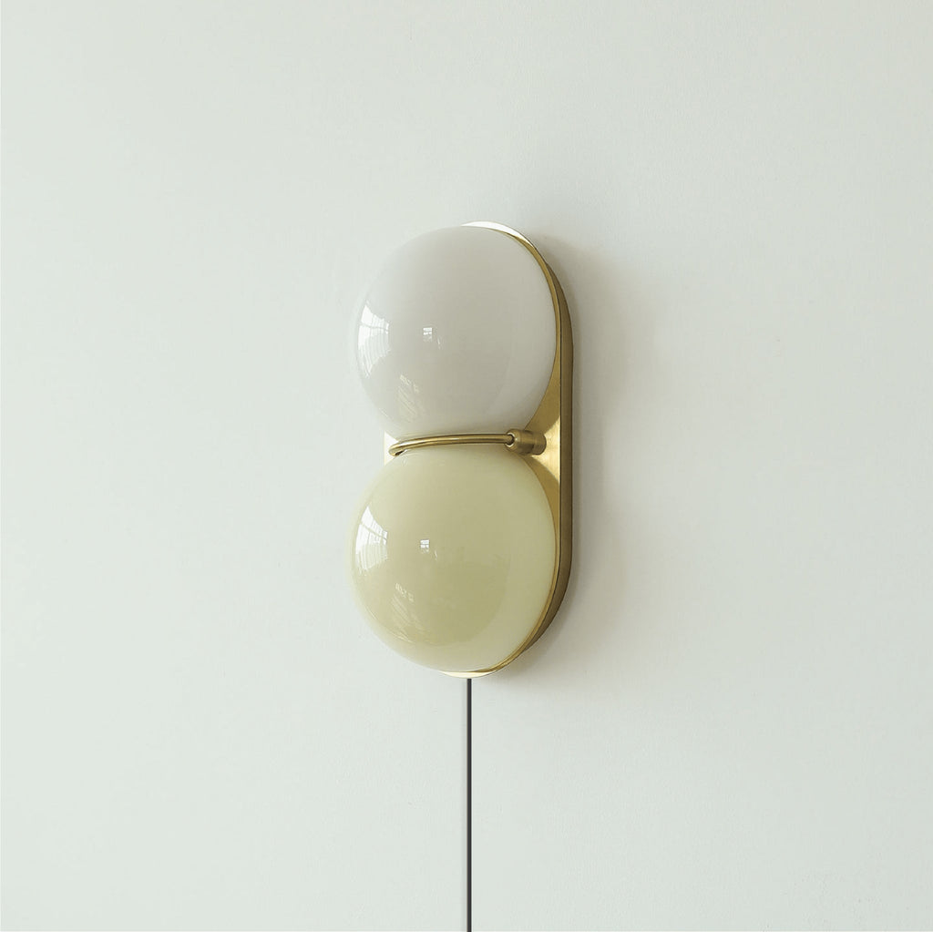 Clérachic wall sconce with a grey-white globe above a pale olive one, on a brass backplate with a cord hanging below.