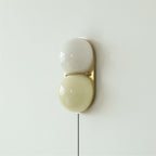 Clérachic wall sconce with a grey-white globe above a pale olive one, on a brass backplate with a cord hanging below.