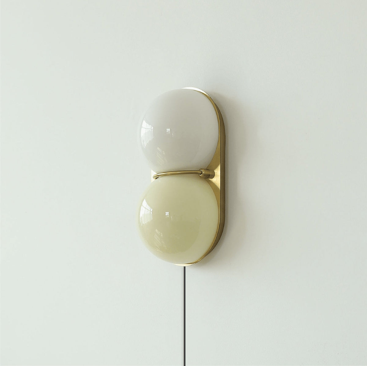 Clérachic wall sconce with a grey-white globe above a pale olive one, on a brass backplate with a cord hanging below.