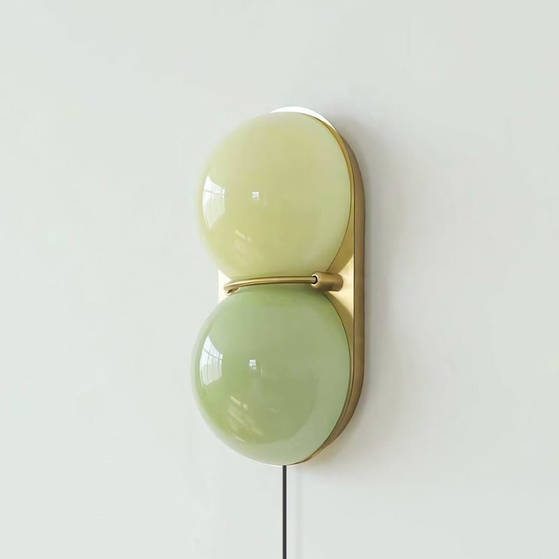 Clérachic wall sconce in two soft green glass globes, pale lime above and sage below, on a brass backplate.