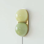 Clérachic wall sconce in two soft green glass globes, pale lime above and sage below, on a brass backplate.