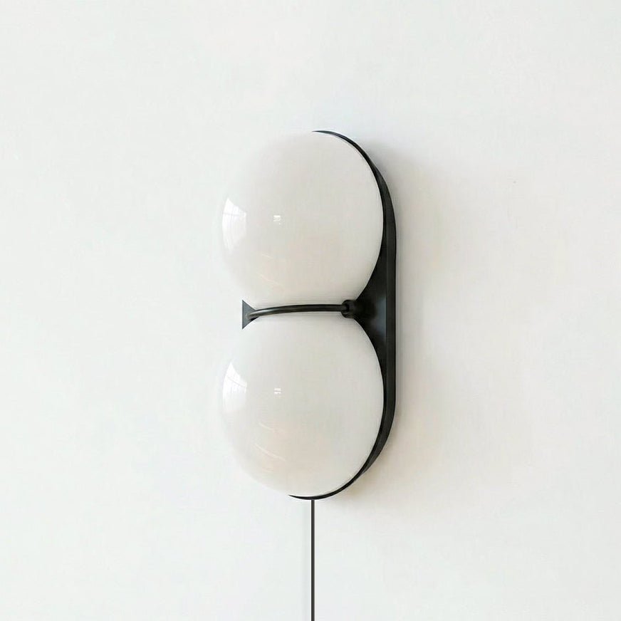 Clérachic two-globe wall sconce in white glass on a black backplate, joined by a slim black band, against a pale wall.