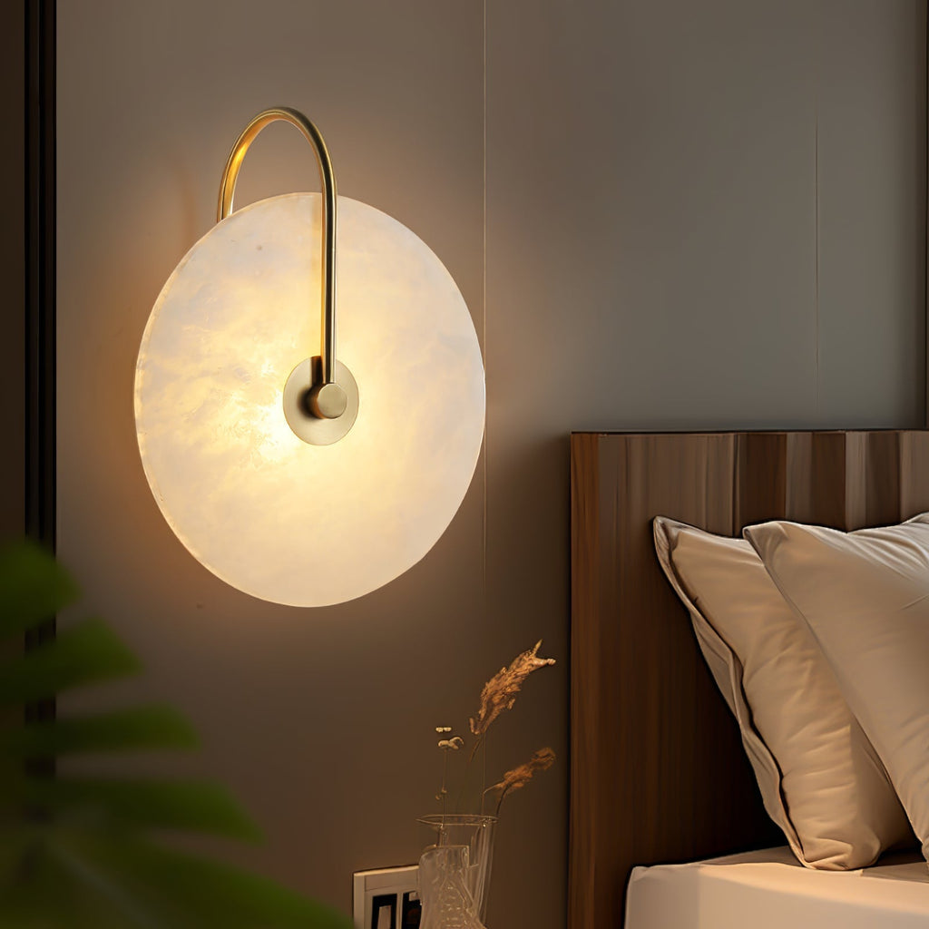Clérachic Plug-In Wall Sconce glows beside a fluted wood headboard, gold arm over the alabaster globe shade in a bedroom.