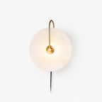 Studio shot of the Clérachic Plug-In Wall Sconce on white, gold arm lit and a black cord trailing from the alabaster disc.