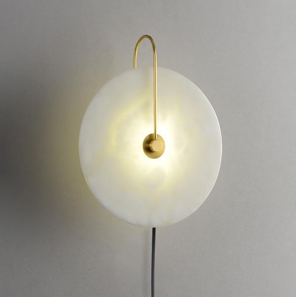 Clérachic Plug-In Wall Sconce close-up, warm light spreading through the alabaster globe shade from the gold centre hub.