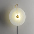 Clérachic Plug-In Wall Sconce close-up, warm light spreading through the alabaster globe shade from the gold centre hub.