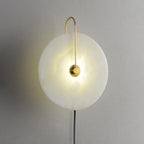 Clérachic Plug-In Wall Sconce close-up, warm light spreading through the alabaster globe shade from the gold centre hub.