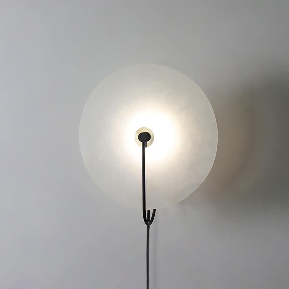 Clérachic Plug-In Wall Sconce in black, the stone disc glowing while the black cord drops straight to the outlet.