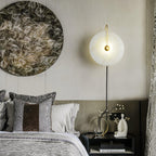 Clérachic Plug-In Wall Sconce lit above a black nightstand, gold arm beside a large round artwork in a paneled bedroom.