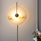 Angled view of the lit Clérachic Plug-In Wall Sconce on a pale wall, pink and white flowers soft in the foreground.
