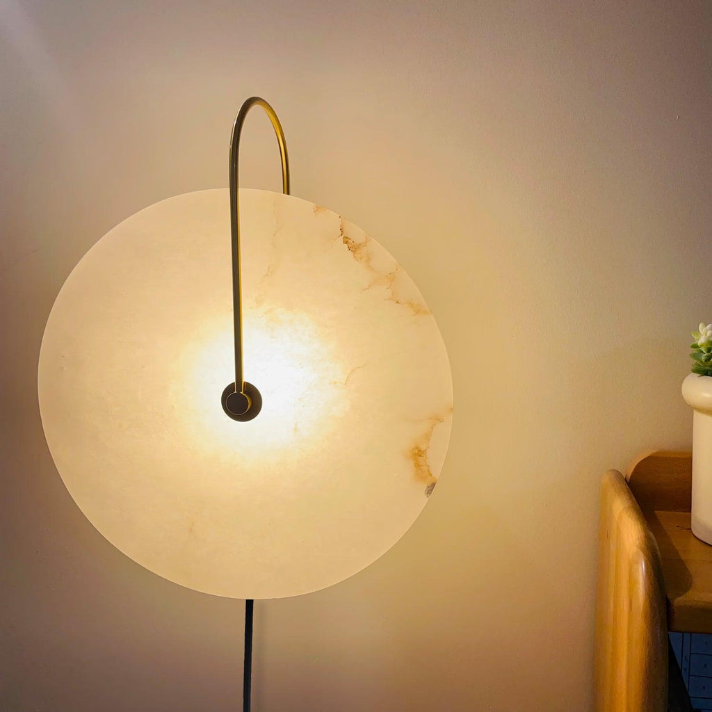 Clérachic Plug-In Wall Sconce lit beside a wood headboard, amber veining visible across the alabaster globe shade.
