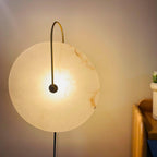 Clérachic Plug-In Wall Sconce lit beside a wood headboard, amber veining visible across the alabaster globe shade.