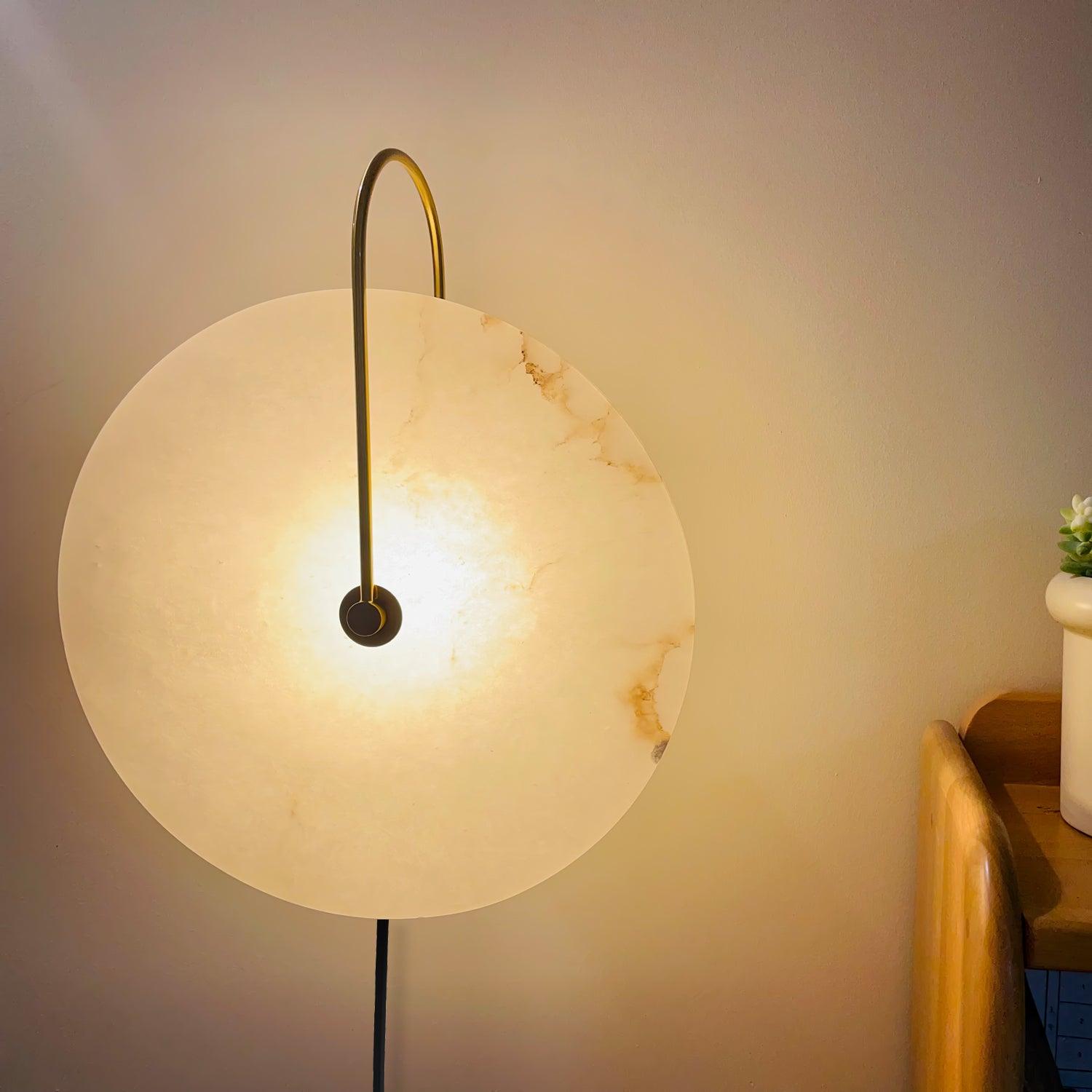 Clérachic Plug-In Wall Sconce lit beside a wood headboard, amber veining visible across the alabaster globe shade.
