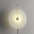 Clérachic Plug-In Wall Sconce lit against a textured grey wall, cloudy alabaster pattern showing in the warm glow.