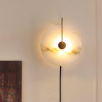 Clérachic Plug-In Wall Sconce with dark veining across the lit alabaster disc, a warm halo cast on the cream wall.