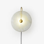 Clérachic Plug-In Wall Sconce on a plain grey backdrop, gold arm and a gently lit alabaster globe shade.