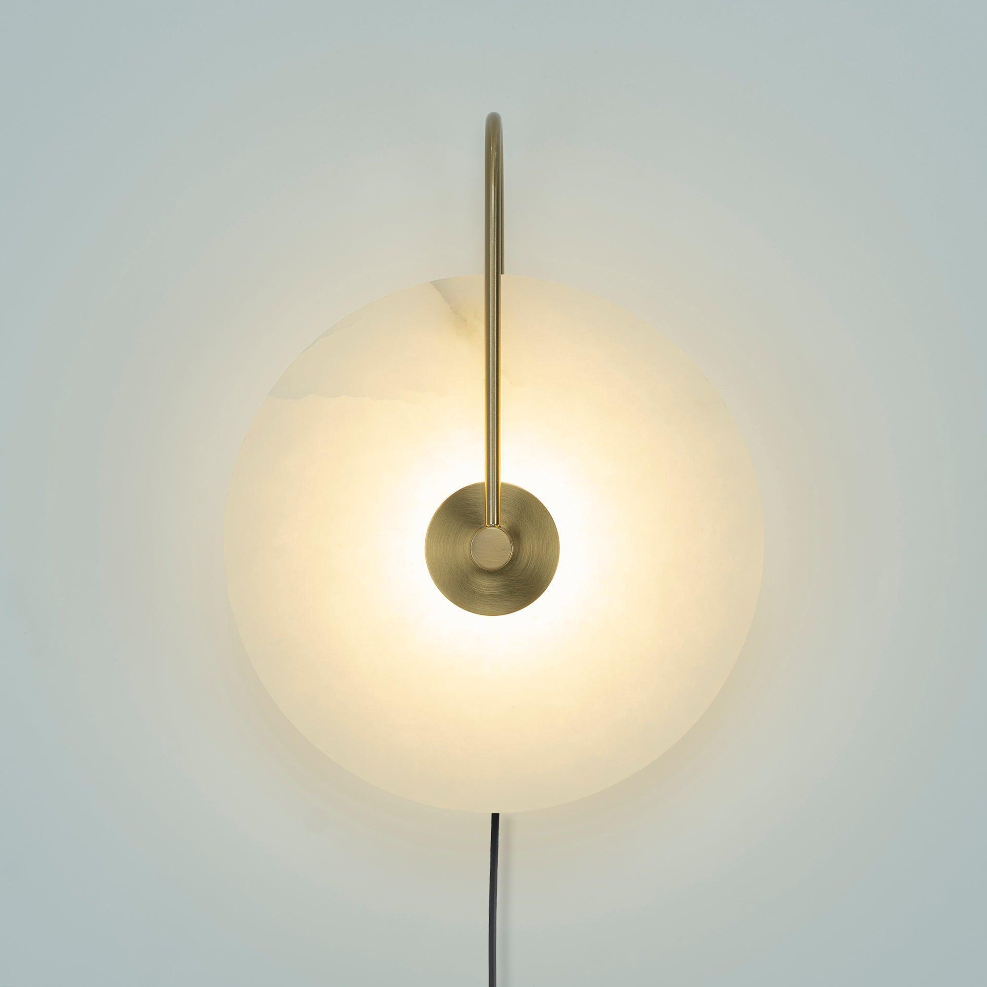 Clérachic Plug-In Wall Sconce lit against a pale backdrop, the long gold arm reaching over the alabaster globe shade.
