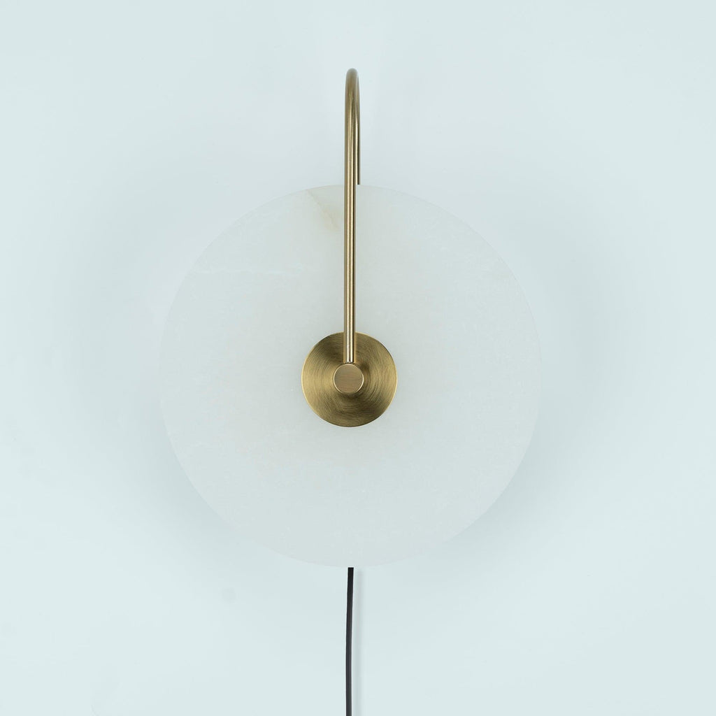 Unlit Clérachic Plug-In Wall Sconce on a pale backdrop, showing translucent alabaster and an antique-gold central hub.