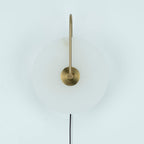 Unlit Clérachic Plug-In Wall Sconce on a pale backdrop, showing translucent alabaster and an antique-gold central hub.