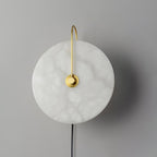 Unlit Clérachic Plug-In Wall Sconce on a grey wall, gold arm arching over the cloudy white alabaster globe shade.