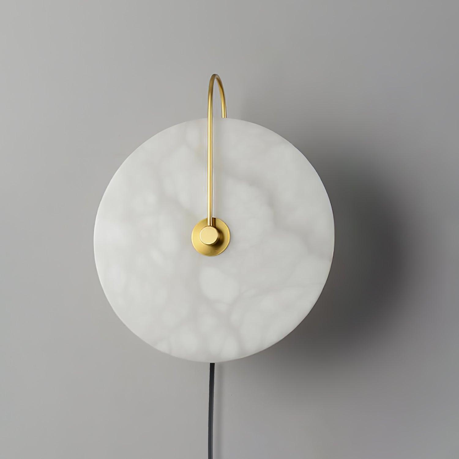 Unlit Clérachic Plug-In Wall Sconce on a grey wall, gold arm arching over the cloudy white alabaster globe shade.