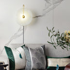 Clérachic Plug-In Wall Sconce lit above a sofa on a marble-veined wall, green cushions and a plant in the living room.