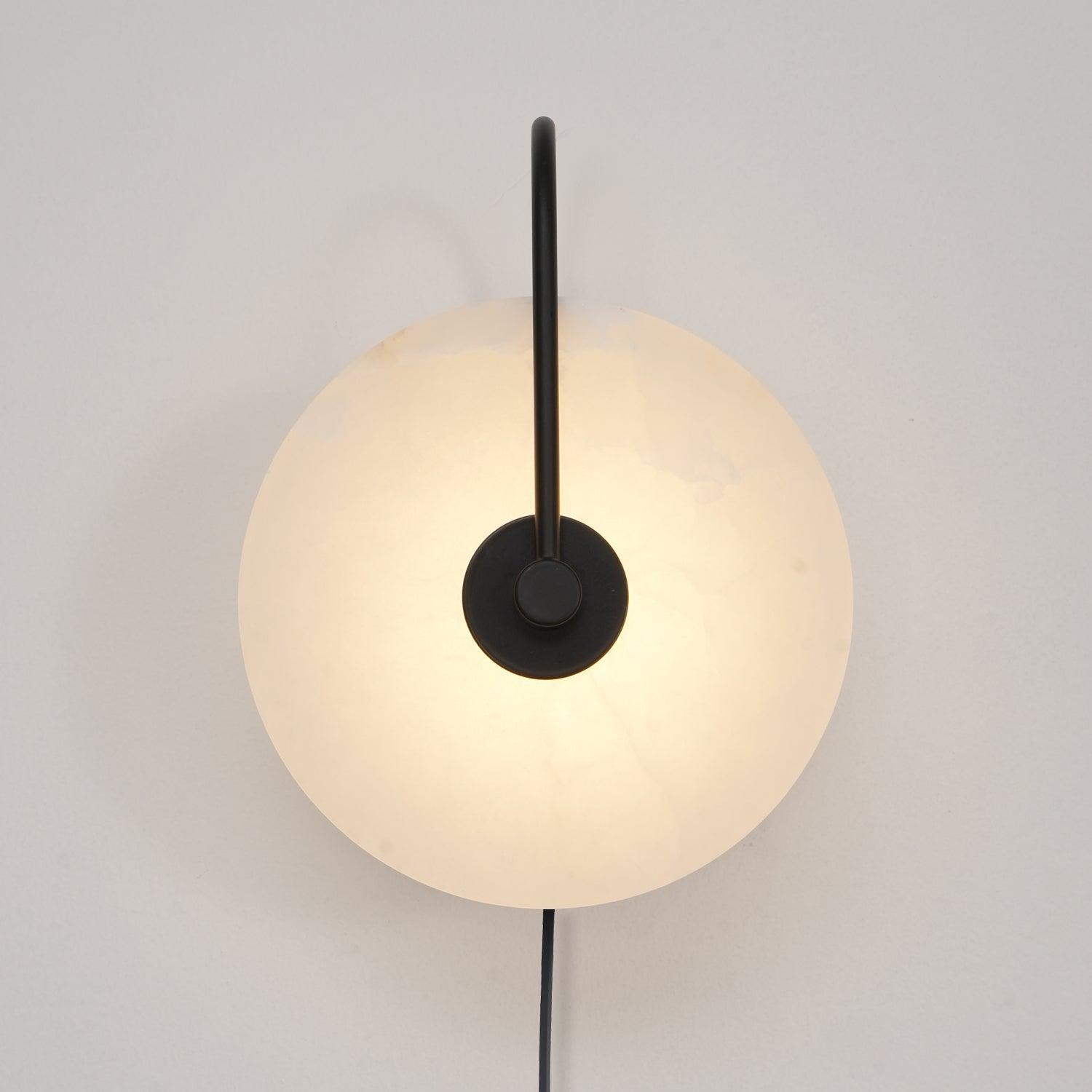 Black-arm Clérachic Plug-In Wall Sconce lit on an off-white wall, matte hardware crossing the mottled alabaster disc.