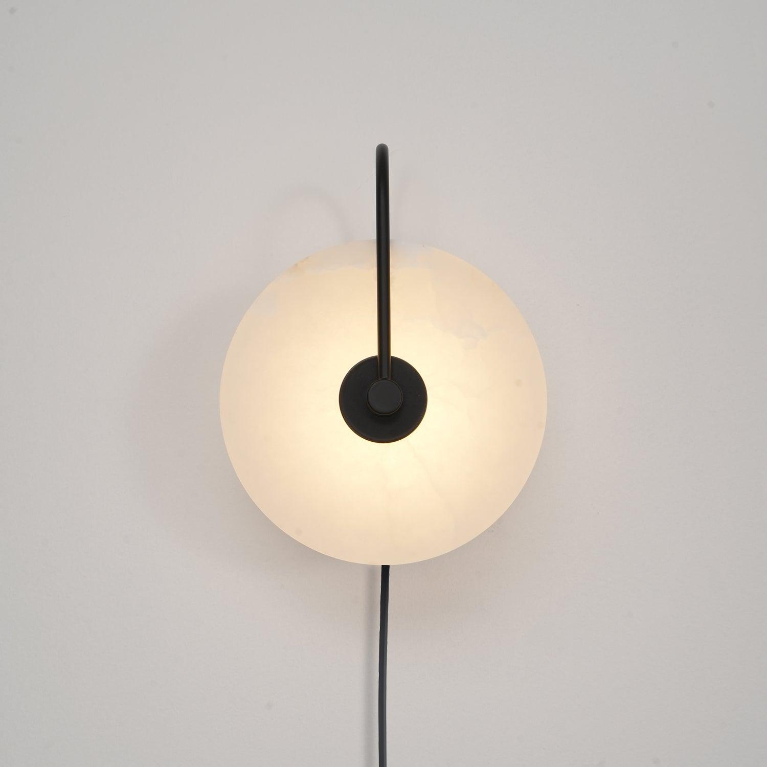 Head-on Clérachic Plug-In Wall Sconce in black on a white wall, slim vertical arm and grey veining in the lit disc.