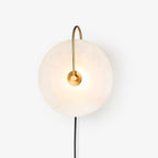 White-studio Clérachic Plug-In Wall Sconce with a gold J-hook arm, black cord hanging from the glowing stone disc.