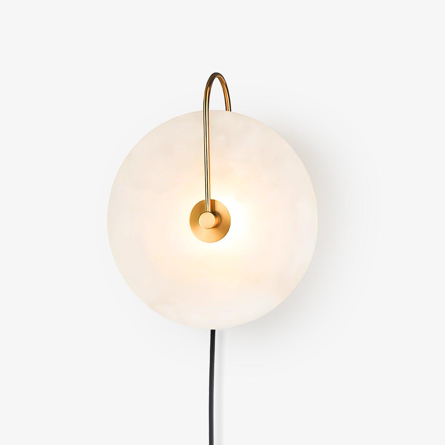 White-studio Clérachic Plug-In Wall Sconce with a gold J-hook arm, black cord hanging from the glowing stone disc.
