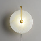 Satin-gold Clérachic Plug-In Wall Sconce on a finely textured grey wall, tan veining lit through the alabaster disc.