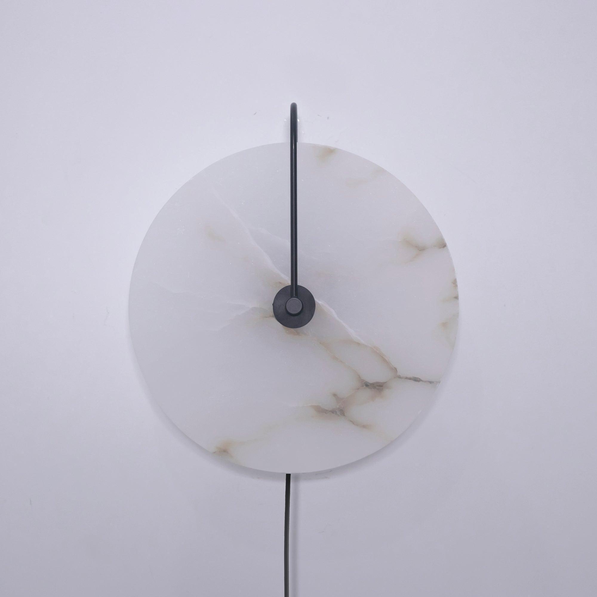 Unlit black-finish Clérachic Plug-In Wall Sconce on grey, beige and brown veining across the pale alabaster globe shade.
