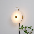 Clérachic Plug-In Wall Sconce glowing on a white wall, gold hook arm holding the warm alabaster globe shade in place.