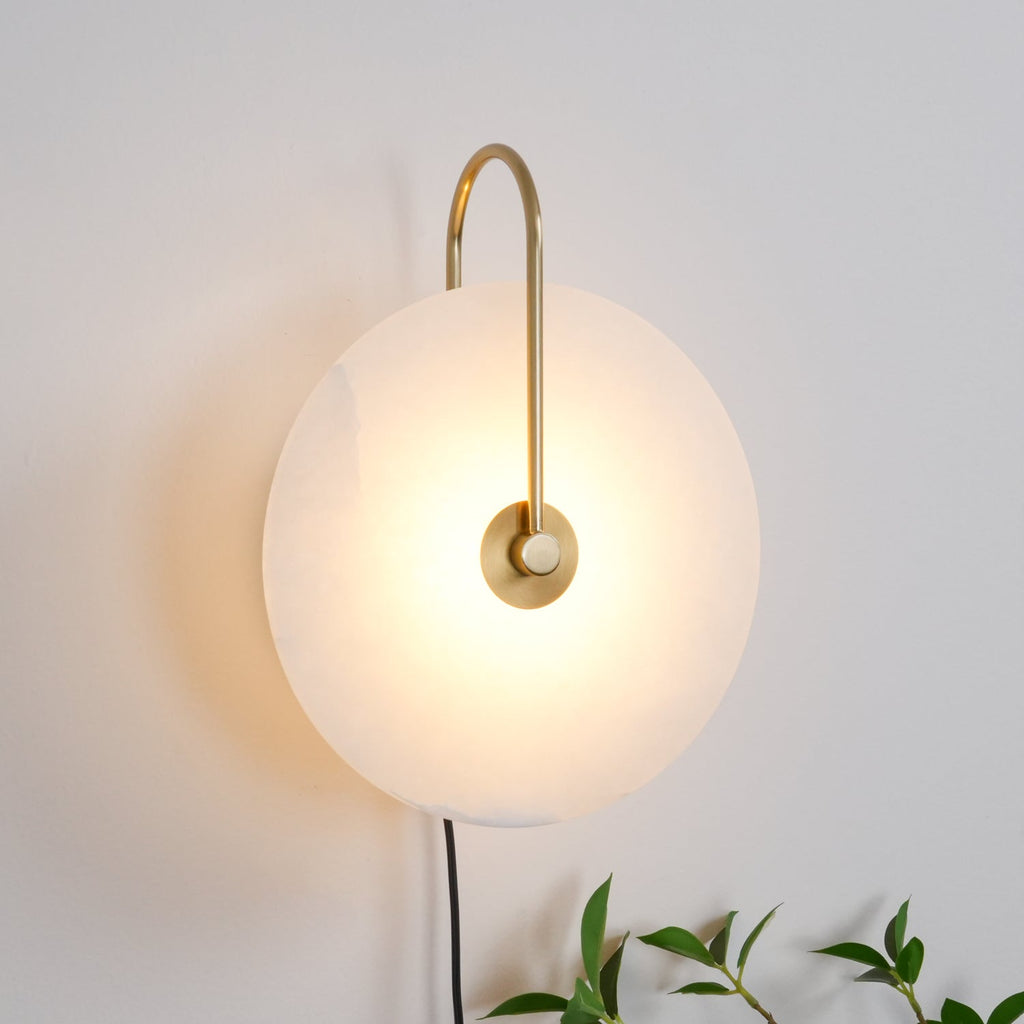 Clérachic Plug-In Wall Sconce on a light grey wall, gold U-shaped arm and glowing disc with leafy sprigs at the corner.